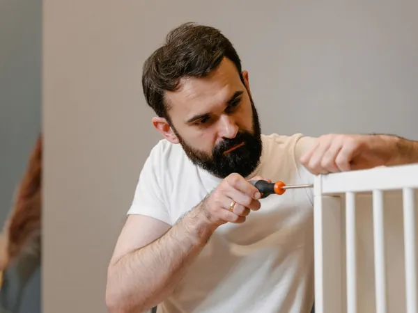 Hombre montando un mueble de madera blanca con un destornillador