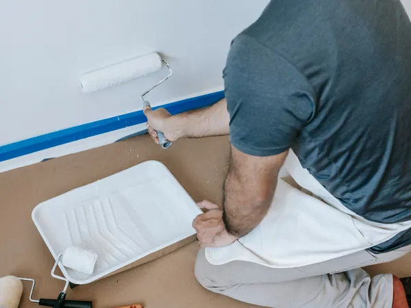 Hombre pintando una pared con rodillo con el suelo protegido